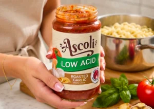 Woman holding jar of Ascoli Low Acid pasta sauce while cooking dinner in the kitchen